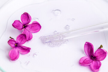 Pipette with serum, oil, gel with lilac flowers on white background. Skin care, natural beauty products concept. Closeup
