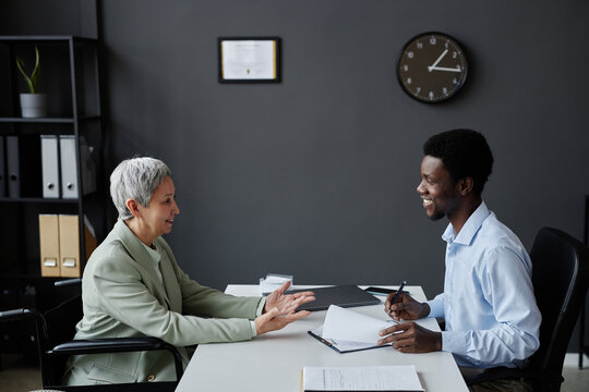 Side view portrait of smiling senior woman with disability speaking to HR recruiter in job interview