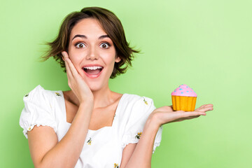 Photo of adorable impressed lady wear white crop top arm cheek holding small cupcake isolated green color background