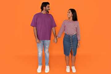Happy loving eastern couple holding hands on orange background