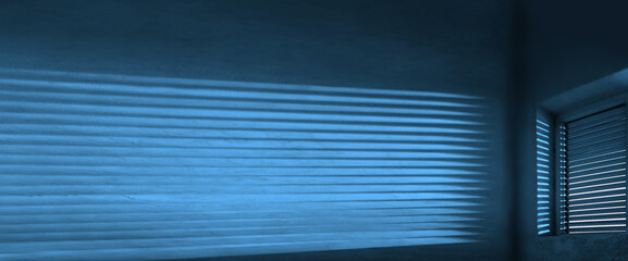 interior of the dark room.The shadow of the sunset falling on the wall through the louvers. Light from the lamp and shadow on the room wall from roller window shutter. night scene.
