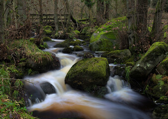 The Bar Brook with Water Cascading Over Rocks with an Old Wooden Foot Bridge in the Peak District