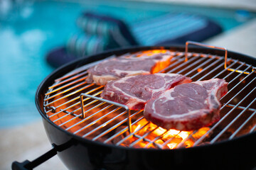 entrec&ocirc;te, pi&egrave;ce de viande qui grille sur un barbecue avec une piscine en arri&egrave;re-plan. Symbole des vacances et de la d&eacute;tente
