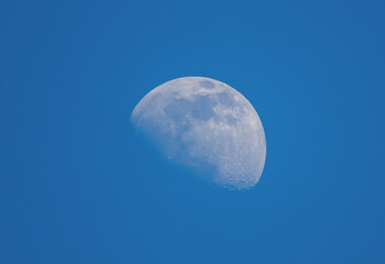A close-up of the moon seen during the day against a blue sky background