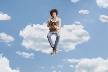 Obraz premium Young man with curly hair sitting on a cloud and holding a book