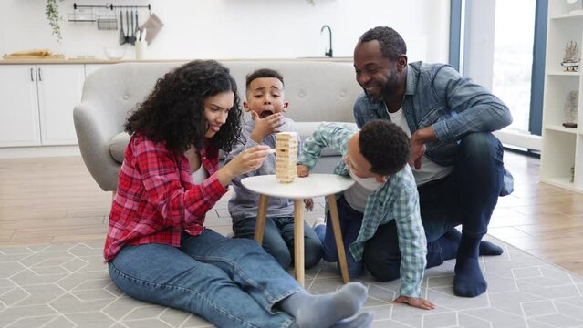 Four-person family playing board game with wooden blocks on small table in living room. Happy people being engaged in enjoyable activity showing importance of love and care.