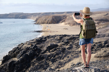 A tourist woman taking a picture from a cliff on the coastline in Lanzarote, Canary Islands.