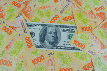 100 dollar bill surrounded by 1,000 Argentinian peso banknotes