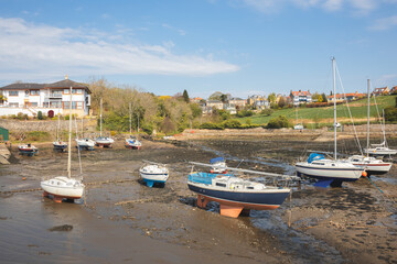 Fototapeta na wymiar Sunny day along the shoreline of the Fife Coastal Path at Black Sands Beach at low tide and beached sailboats on the Firth of Forth at Aberdour Harbour, Burntisland, Scotland, UK.