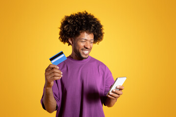 Positive mature black curly man in purple t-shirt recommends credit card, uses smartphone for...