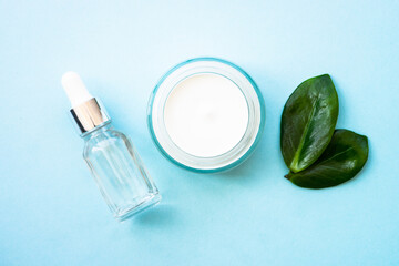 Natural cosmetic products on blue. Cream and serum bottlr with green leaves. Flat lay, minimal.