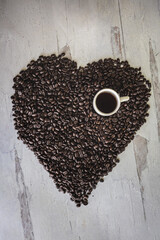 Coffee beans in a heart shape with one small cup of dark espresso flat lay background 