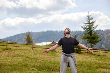 happy caucasian man in a clearing against the backdrop of mountains. He spread his arms and closed his eyes.