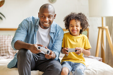 Happy ethnic family father and son playing video game console at home