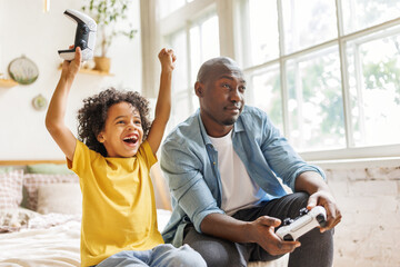 Happy ethnic family father and son playing video game console at home.