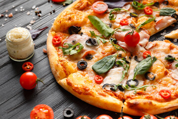 Pizza with jerky, cheese, olives, sauce and spices on a dark wooden background.