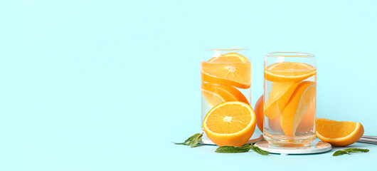 Glasses of orange infused water on light blue background with space for text