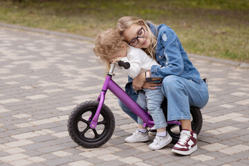 Young mother teaches her little son how to ride a balance bike in the park