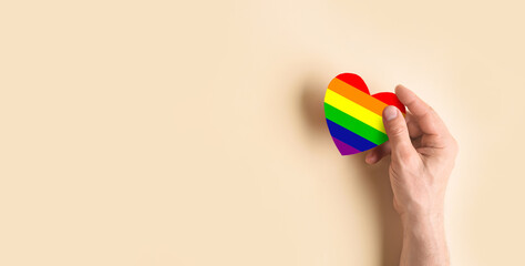 Hand holding rainbow heart on beige background with space for text. LGBT concept