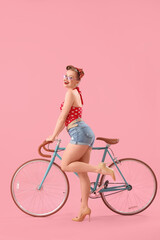 Young pin-up woman with bicycle on pink background