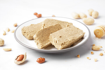 Plate with slices of tasty halva and peanuts on white background