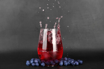 Glass of tasty blueberry cider with splashes, ice cube and berries on dark background
