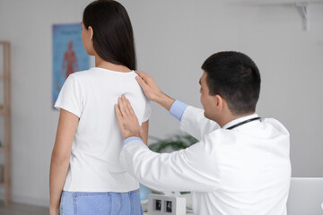 Male doctor checking posture of young woman in clinic - obrazy, fototapety, plakaty