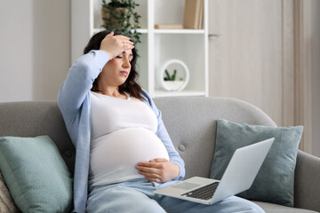 Tired young pregnant woman working with laptop at home