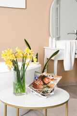 Vase with narcissus flowers and magazine on table in interior of bathroom