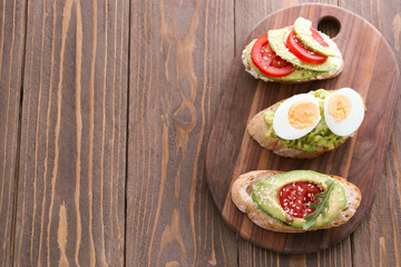 Board of tasty bruschettas with avocado on wooden background