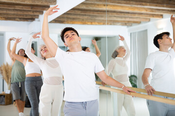Group of dancers doing exercises using ballet barre in a modern fitness studio.
