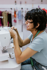 Young latin woman fashion designer working with a sewing machine at her workshop in Mexico Latin...
