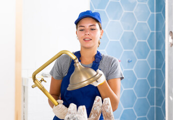 Young woman builder holds a shower head, working in the bathroom during repair