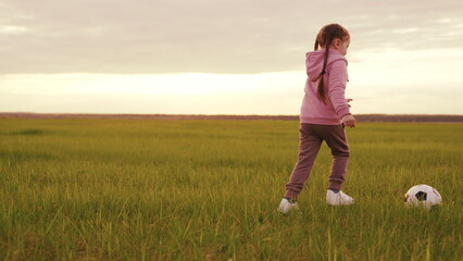 child girl runs across green field sunset kicking ball. children playing soccer ball sunset....