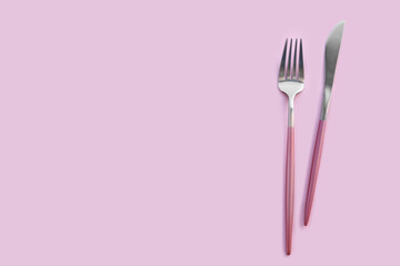 Stainless steel fork and knife on pink background