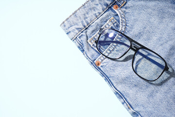 Stylish jeans with black eyeglasses on pale blue background