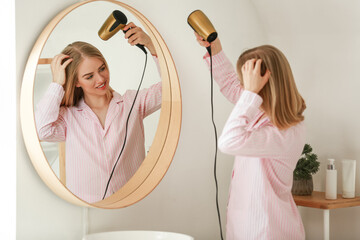 Pretty young woman drying hair in front of mirror