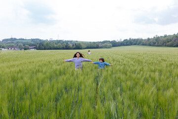 three girls running together in a big field of wheat