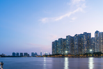 Tall buildings on along riverbank under cloudy sky in evening