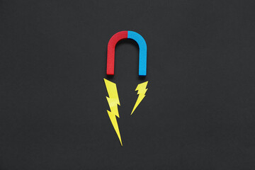 Paper lightnings with horseshoe shaped magnet on black background