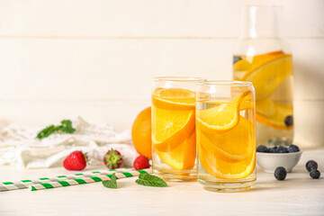 Glasses and bottle of infused water with orange slices on white table