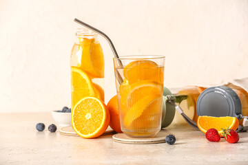 Glass and bottles of infused water with orange slices on white table