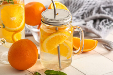 Mason jar and glass of infused water with orange slices on white tile table