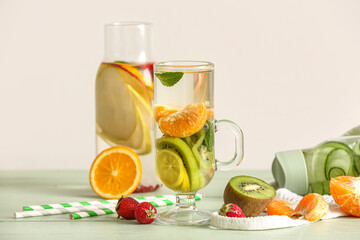 Glass and bottles of infused water with different sliced fruits on grey table