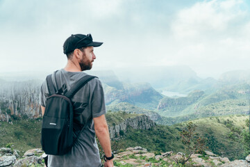 Wide shot of a man on a cliff with a the view from the top of the blyde river canyon in South Africa.