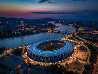 Fototapeta premium Budapest, Hungary - Aerial skyline view of Budapest at dusk, with National Athletics Centre, Rakoczi bridge over River Danube and MOL Campus skyscraper building at background with colorful sunset sky