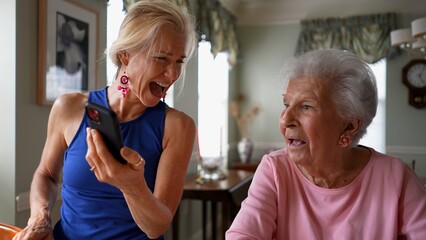 Happy smiling, laughing mature blonde woman holds phone with elderly senior mother having video chat on phone. Smiling blonde lady talking to family on smartphone.