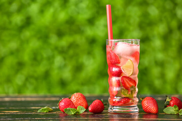 Glass of strawberry lemonade on wooden table outdoors