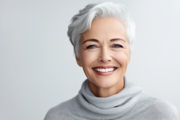 Smiling senior woman in grey sweater looking at camera over white background