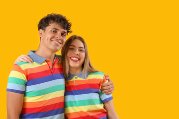 Naklejka premium Young couple in rainbow shirts hugging on yellow background. Pride Month